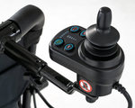 Jazzy Carbon joystick controller mounted on a black attendant control bracket behind the wheelchair