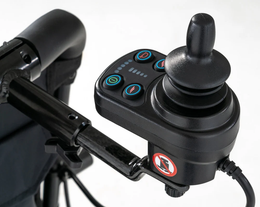 Jazzy Carbon joystick controller mounted on a black attendant control bracket behind the wheelchair